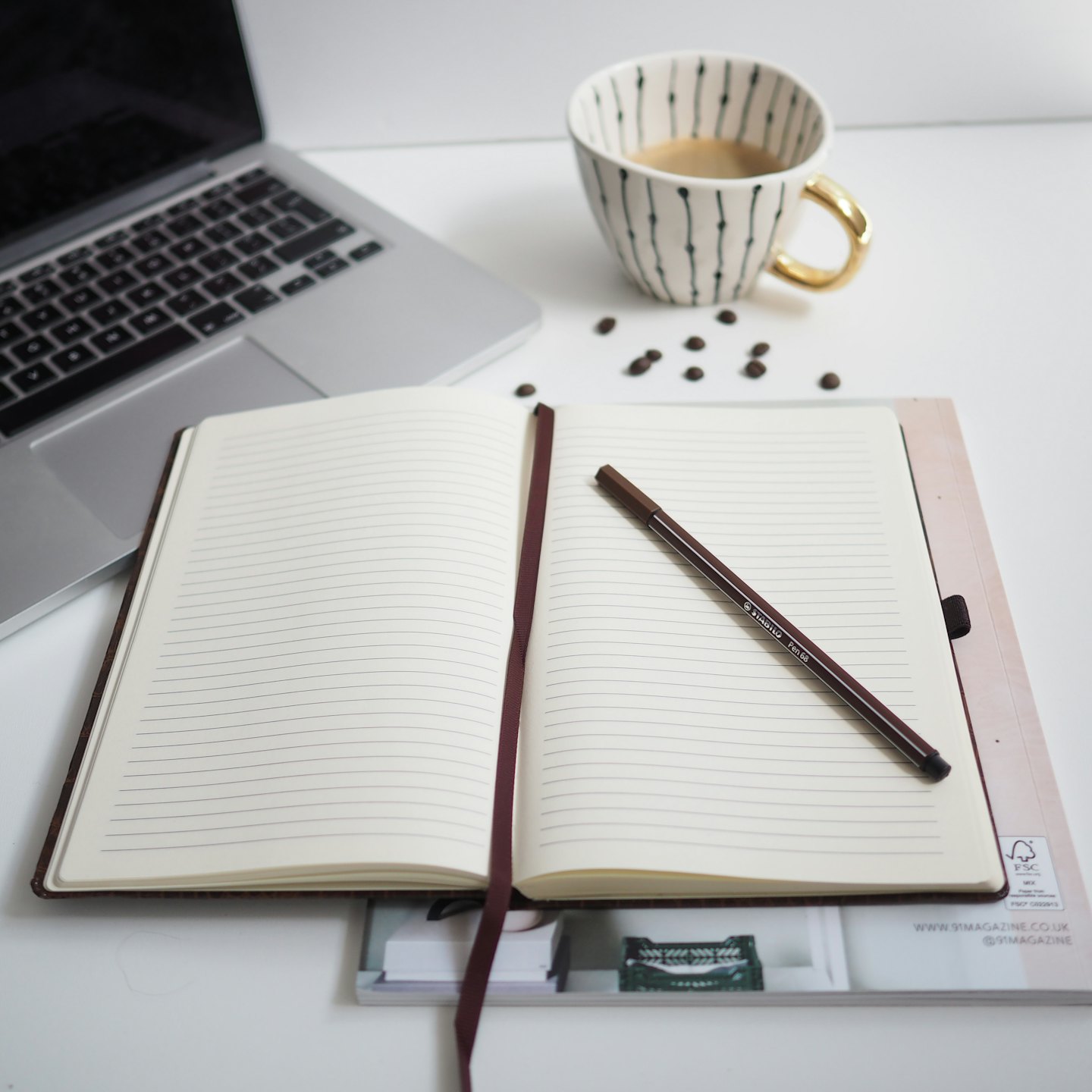 Overhead view of a minimalist desk with a laptop, notebook, and coffee cup.