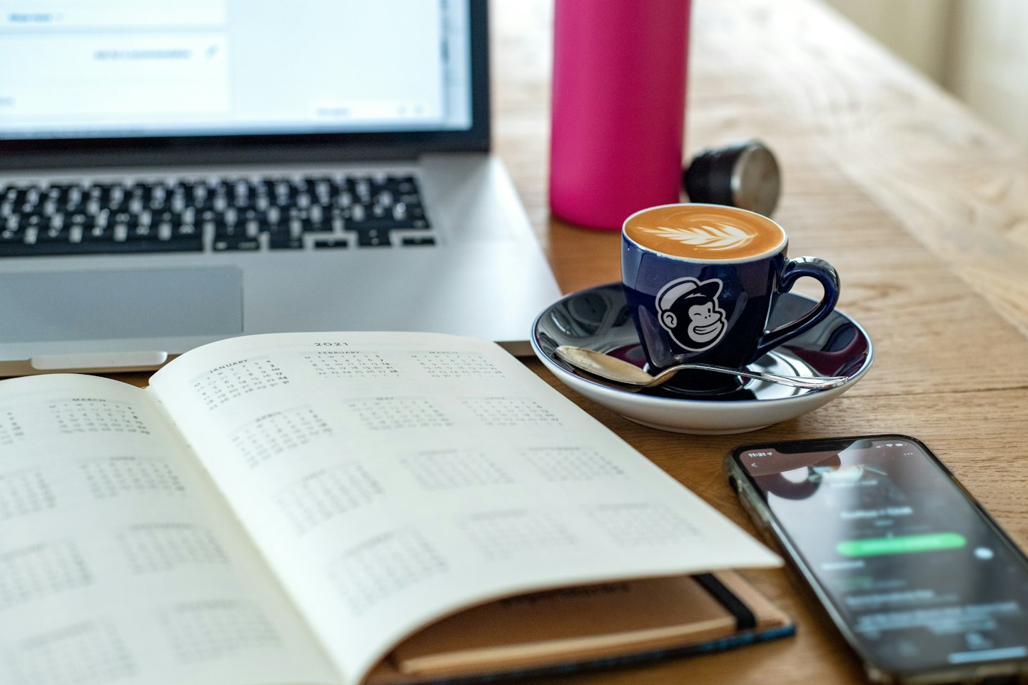 Open planner and smartphone on a wooden desk workstation.